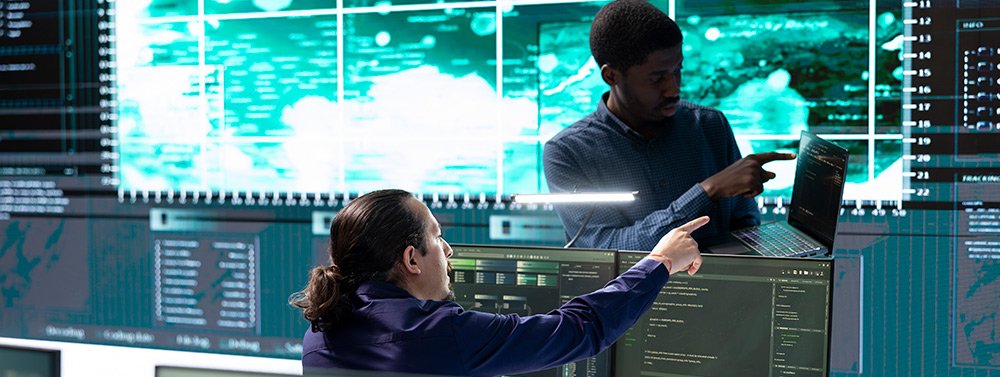 cibserguridad_avanzada_kit_consulting Dos hombres hablando en una sala rodeada de pantallas. Servicio de Cibserseguridad avanzada del Kit Consulting