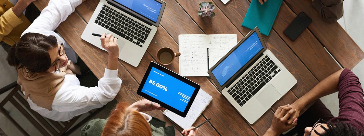 Una mesa con varios ordenadores y personas. Comunicacaciones Unificadas para empresas