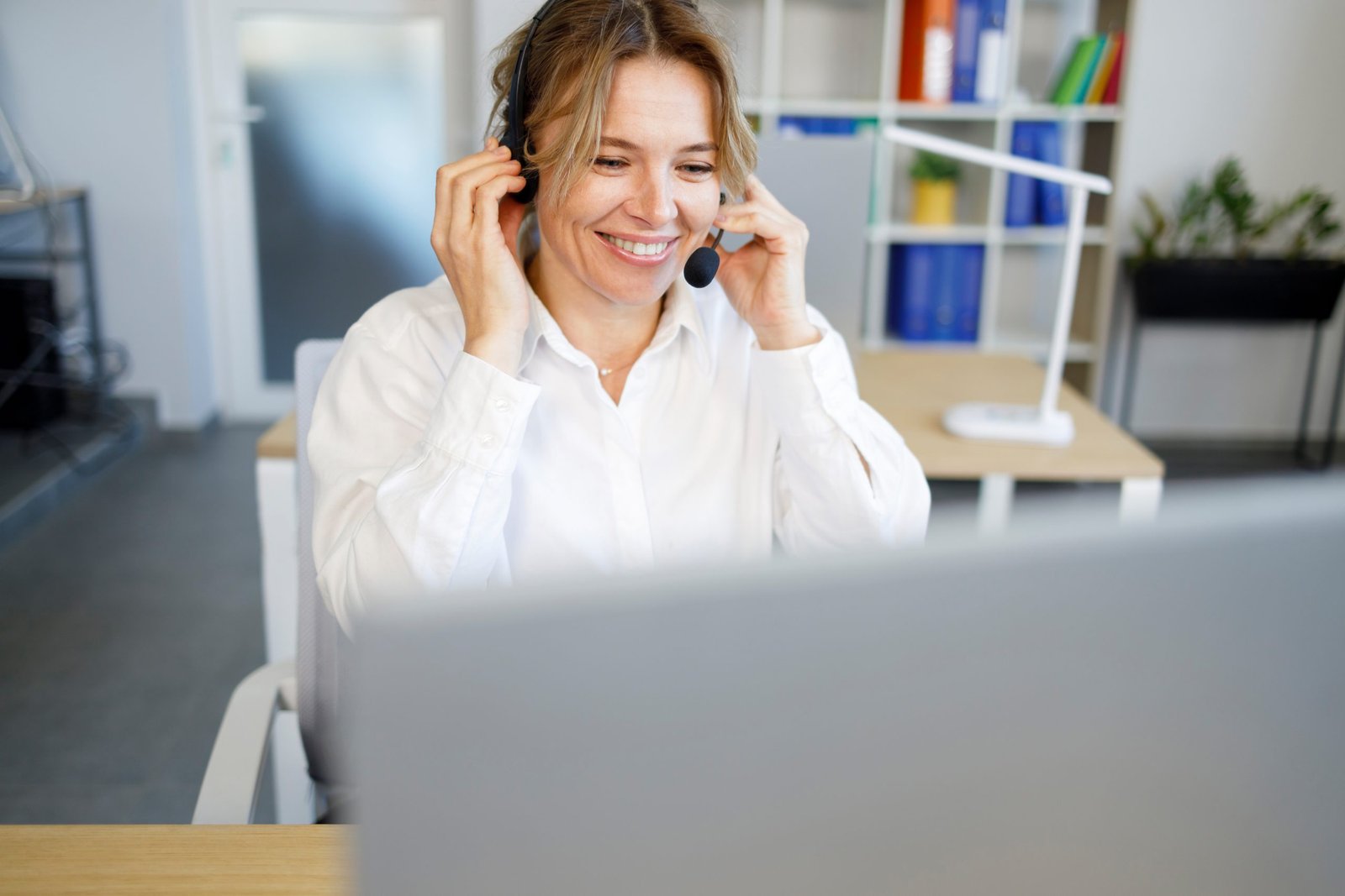 Laughing businesswoman wearing headset talking to caller in customer services department Mujer con auriculares utilizando una Centralita Virtual.